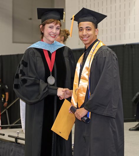 Graduate Tevin Baker shaking hands with college president Betty Reynard.