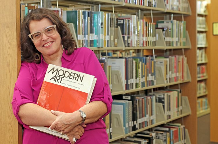Megnet holding a book titled Modern Art while leaning against a library bookshelf.